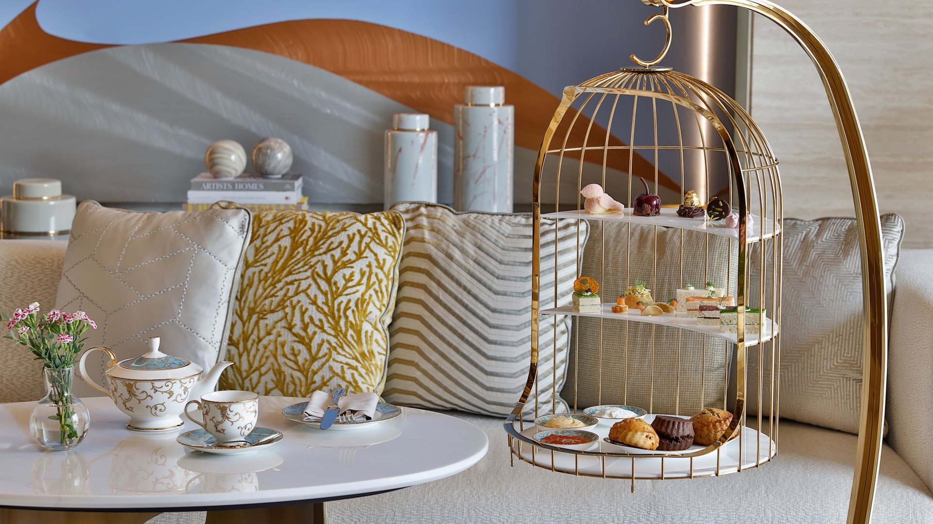 Afternoon tea at The St. Regis Riyadh: a gilded birdcage stand of pastries beside a porcelain teapot