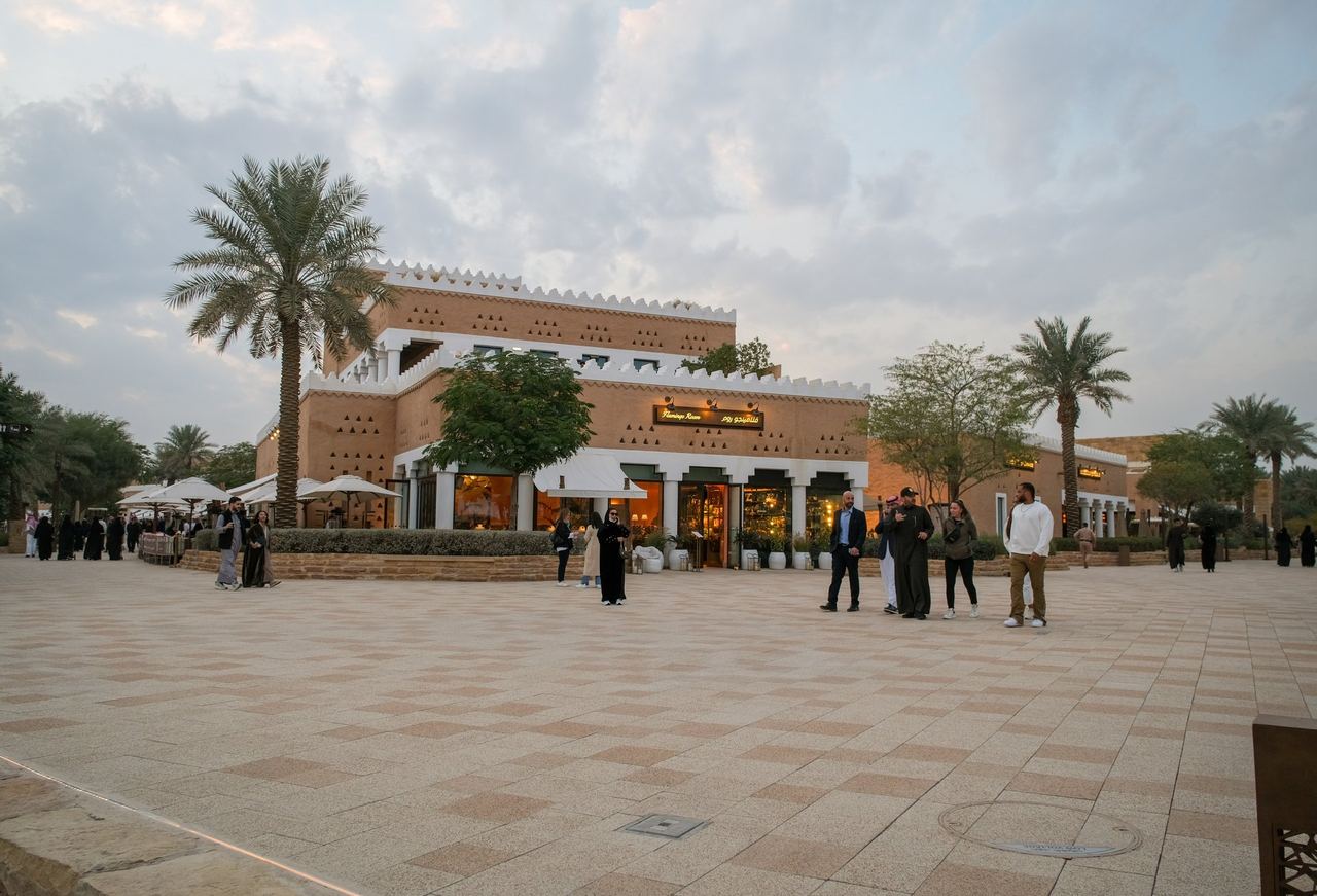 Bujairi Terrace in Diriyah at dusk, its mud-brick restaurants lit behind the palms