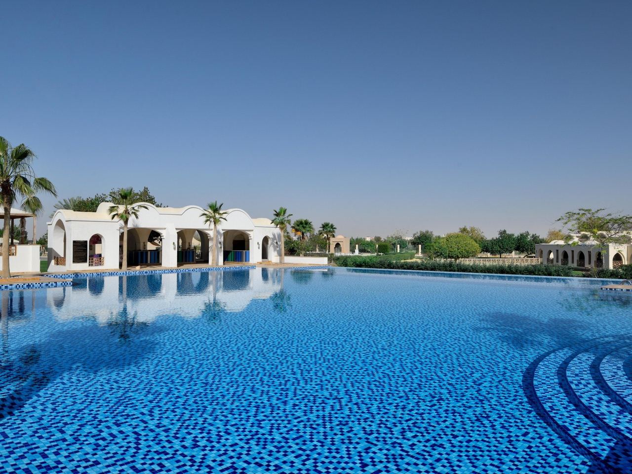 The pool of InterContinental Durrat Al Riyadh Resort & Spa, white arcades and palms beyond the water