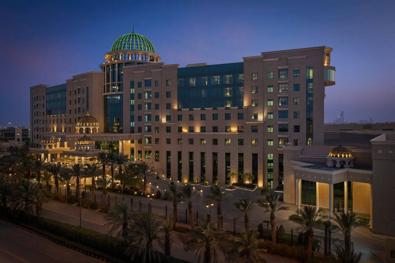 Fairmont Riyadh at dusk, its green glass dome lit above a palm-lined drive