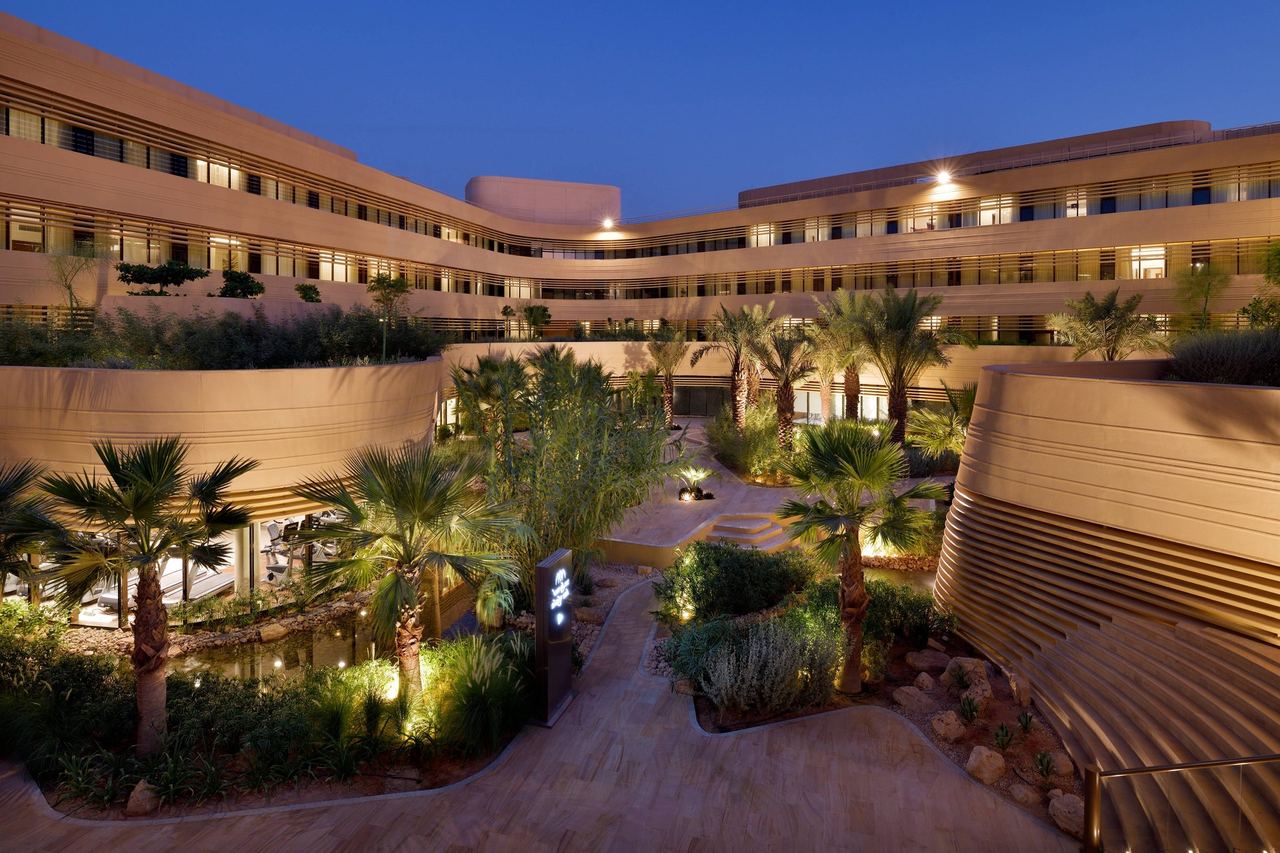 The garden courtyard of Marriott Riyadh Diplomatic Quarter at dusk, palms lit between its curving wings